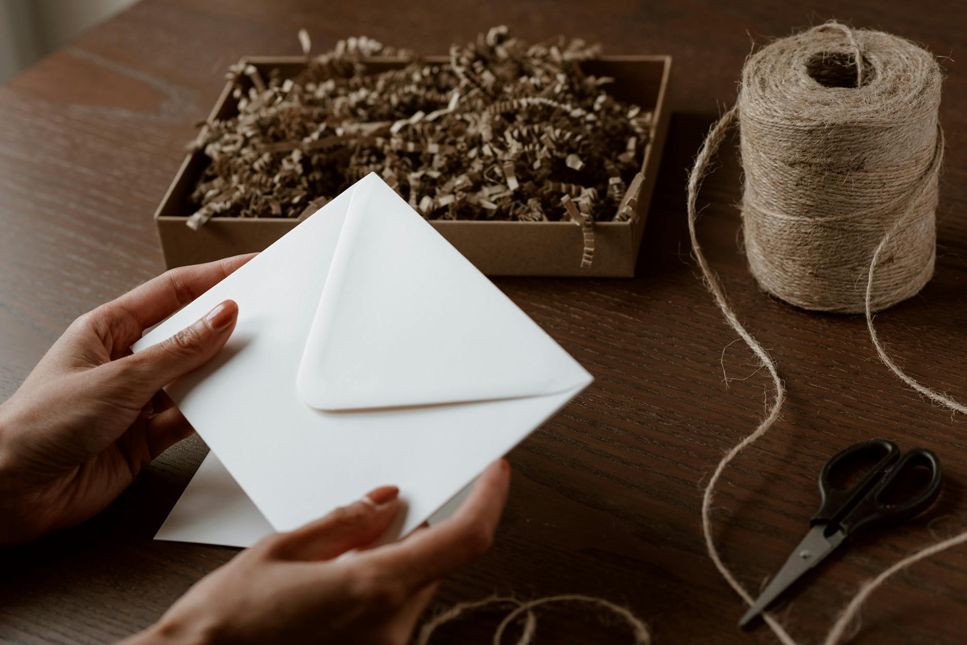 Dłonie tworzące kopertę z recyklingu obok szpuli sznurka i pudełka z wiórami