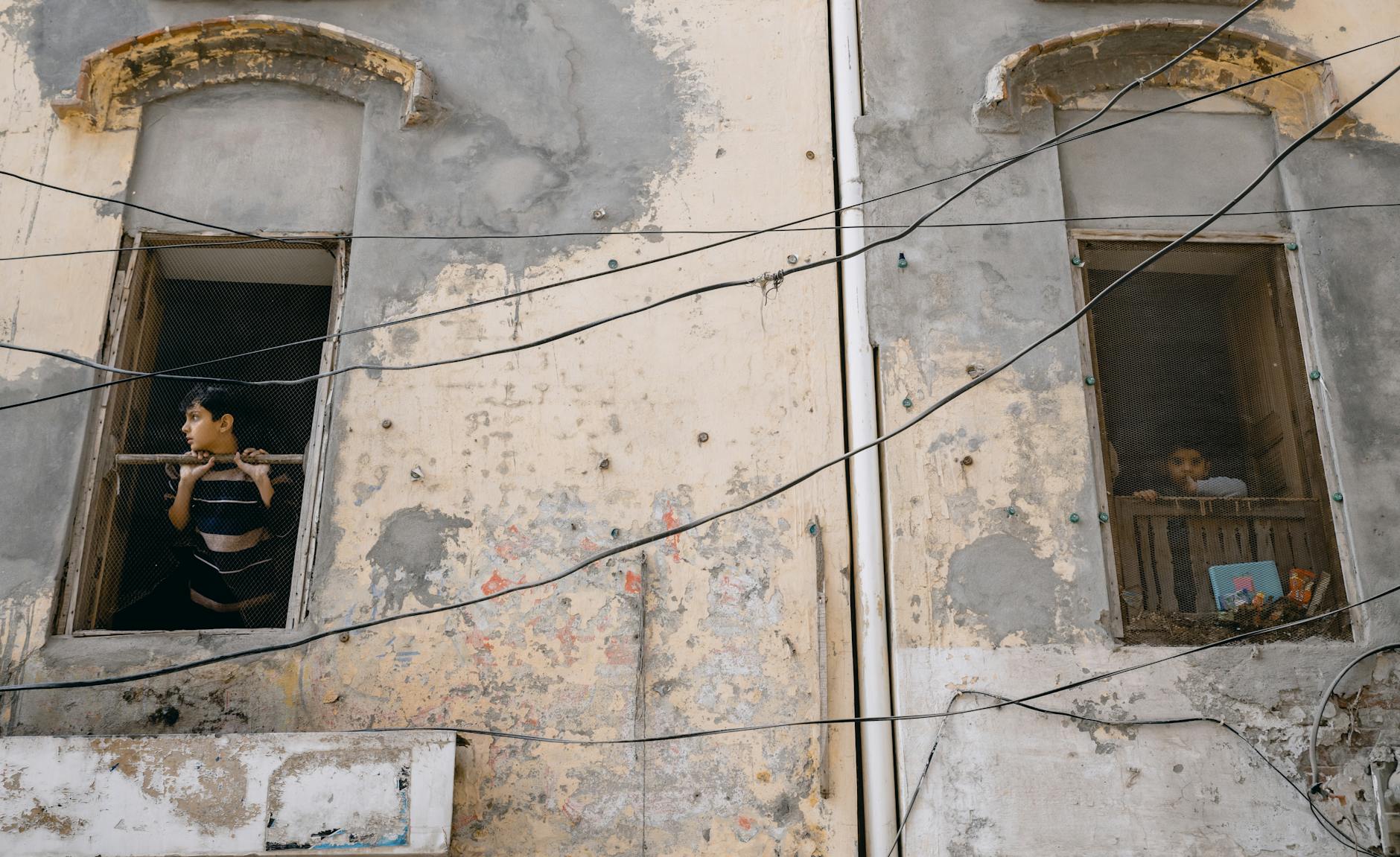 Dwoje dzieci wygląda przez stare okno w zniszczonej kamienicy