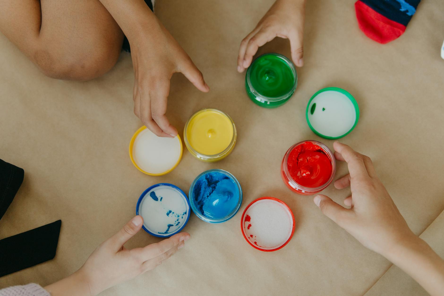 Dziecięce dłonie sięgające po kolorowe słoiczki farb
