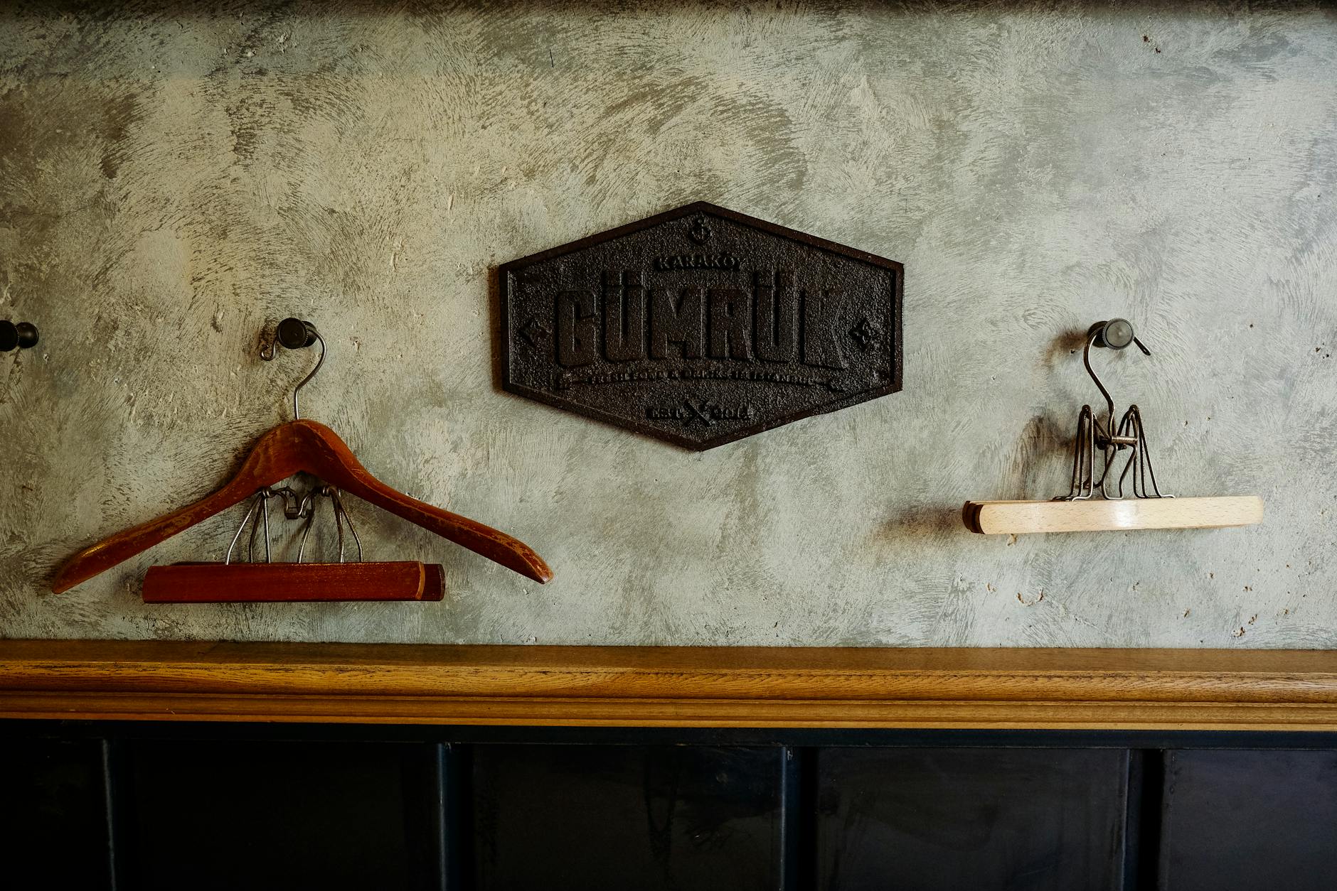 Dwa vintage wieszaki na płaszcze na fakturowanej ścianie pod metalowym szyldem