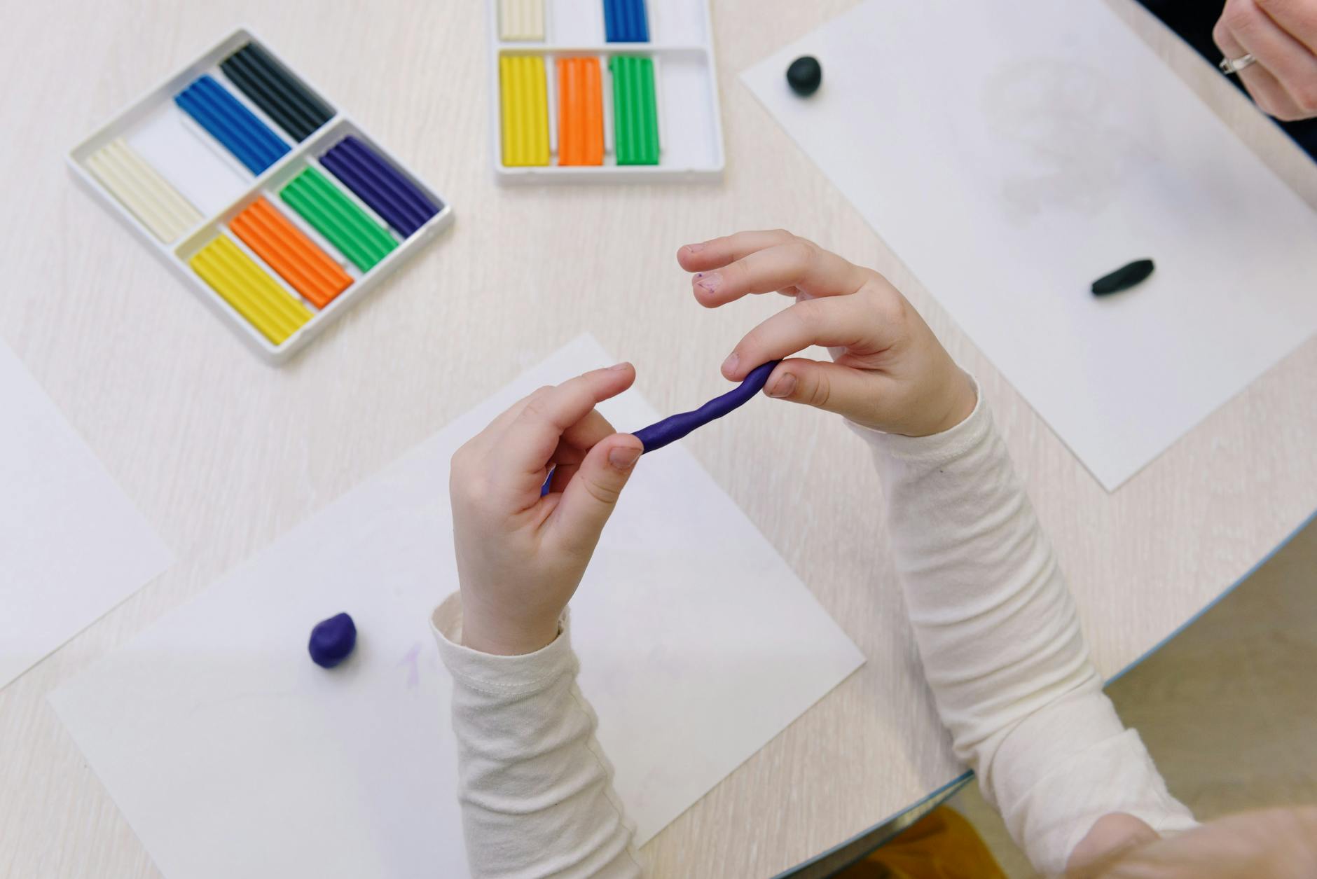 Dziecko lepi fioletową plastelinę w otoczeniu kolorowych wałeczków