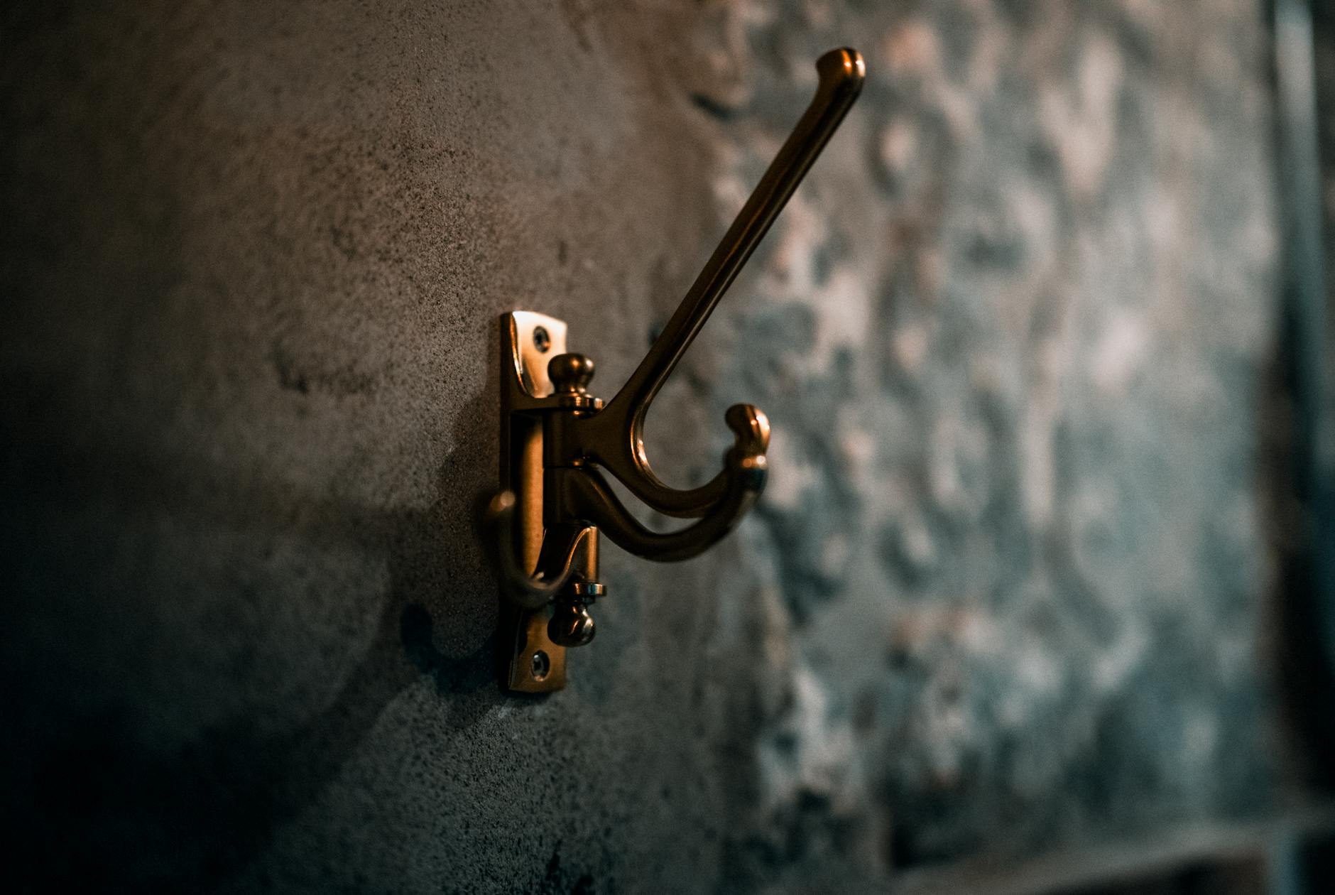 Mosiężny haczyk na płaszcze na fakturowanej ścianie w rustykalnym wnętrzu